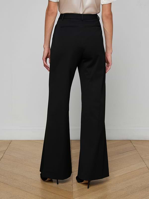 A person stands with their back to the camera, wearing the Pilar Wide-Leg Pant in black and a white top, set against a plain white background.