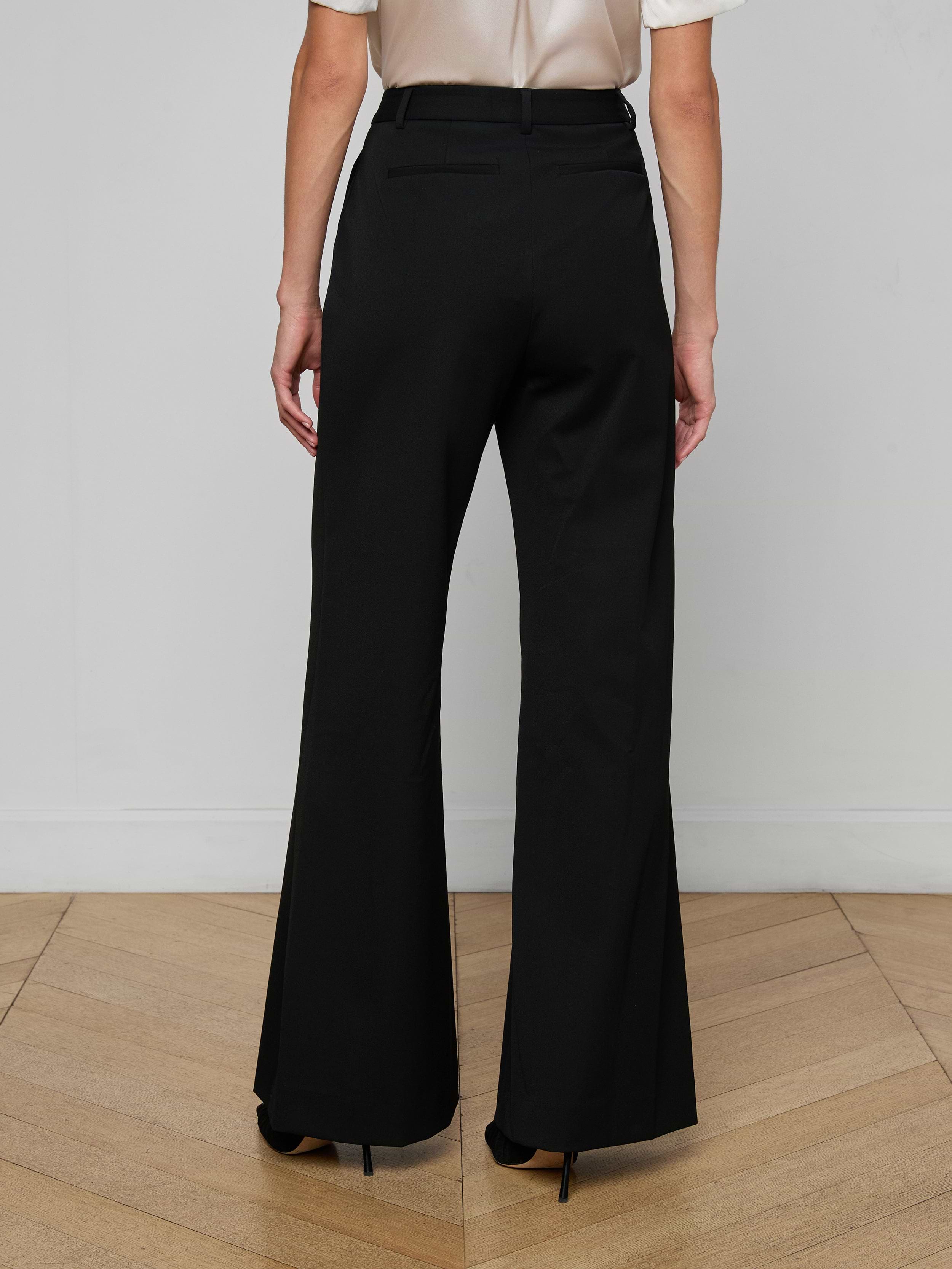 A person stands with their back to the camera, wearing the Pilar Wide-Leg Pant in black and a white top, set against a plain white background.