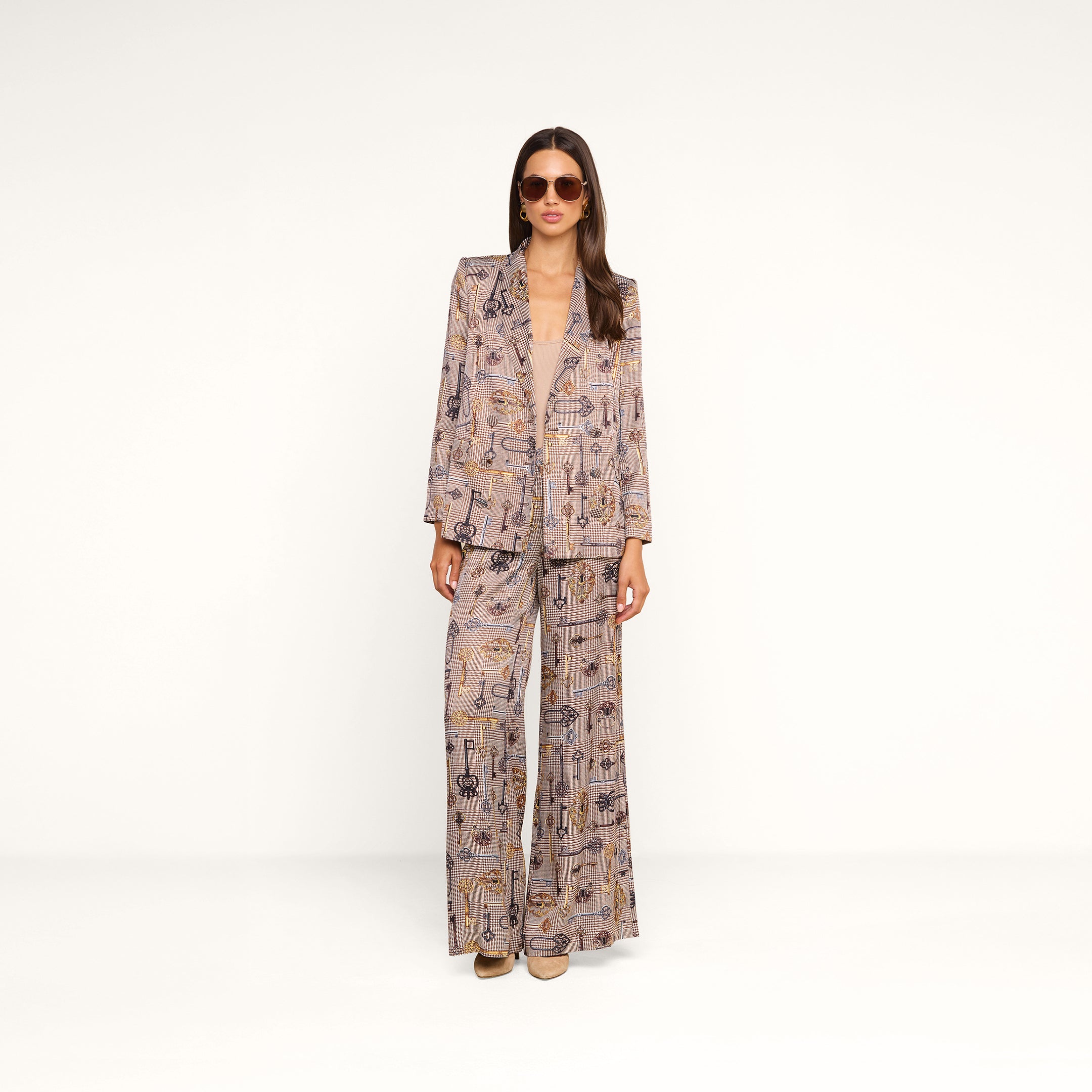 A woman wearing sunglasses and a loose-fitting, patterned suit with a blazer and brown Pilar Wide-Leg Pant stands against a plain white background.