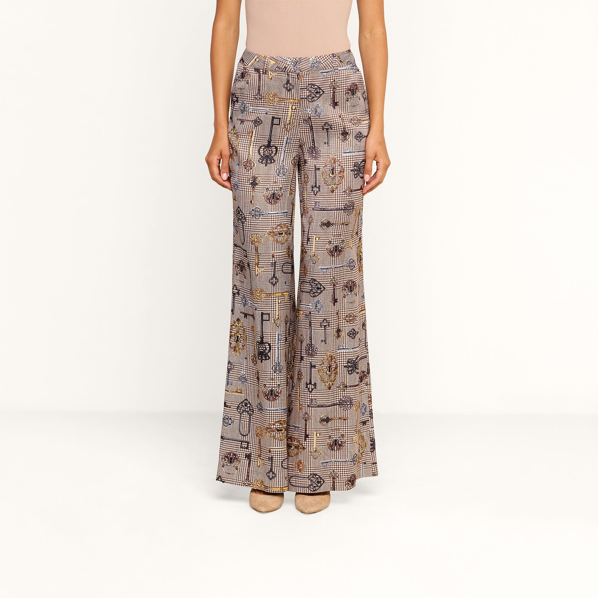 A person wears the Pilar Wide-Leg Pant, featuring a high-waisted brown houndstooth design, paired with a beige top and tan heels, standing against a plain white background.