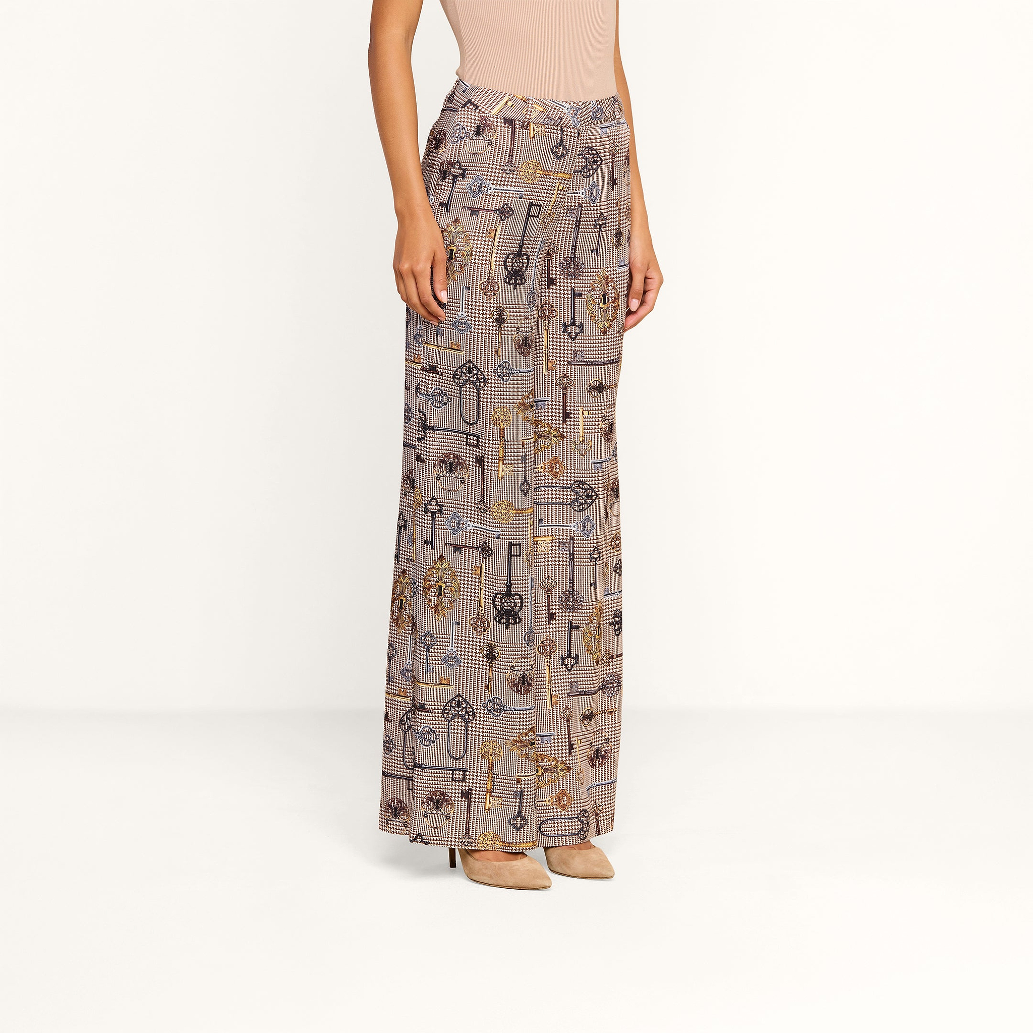 A person wearing the Pilar Wide-Leg Pant—a high-waisted, wide-leg silhouette satin jacquard trouser with various key designs—paired with a sleeveless beige top and beige heels stands against a plain white background.