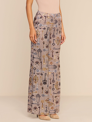 A person wearing the Pilar Wide-Leg Pant, featuring a high-waisted, wide-leg silhouette with a keys and chains pattern, paired with a beige sleeveless top and beige heels, stands against a plain background.