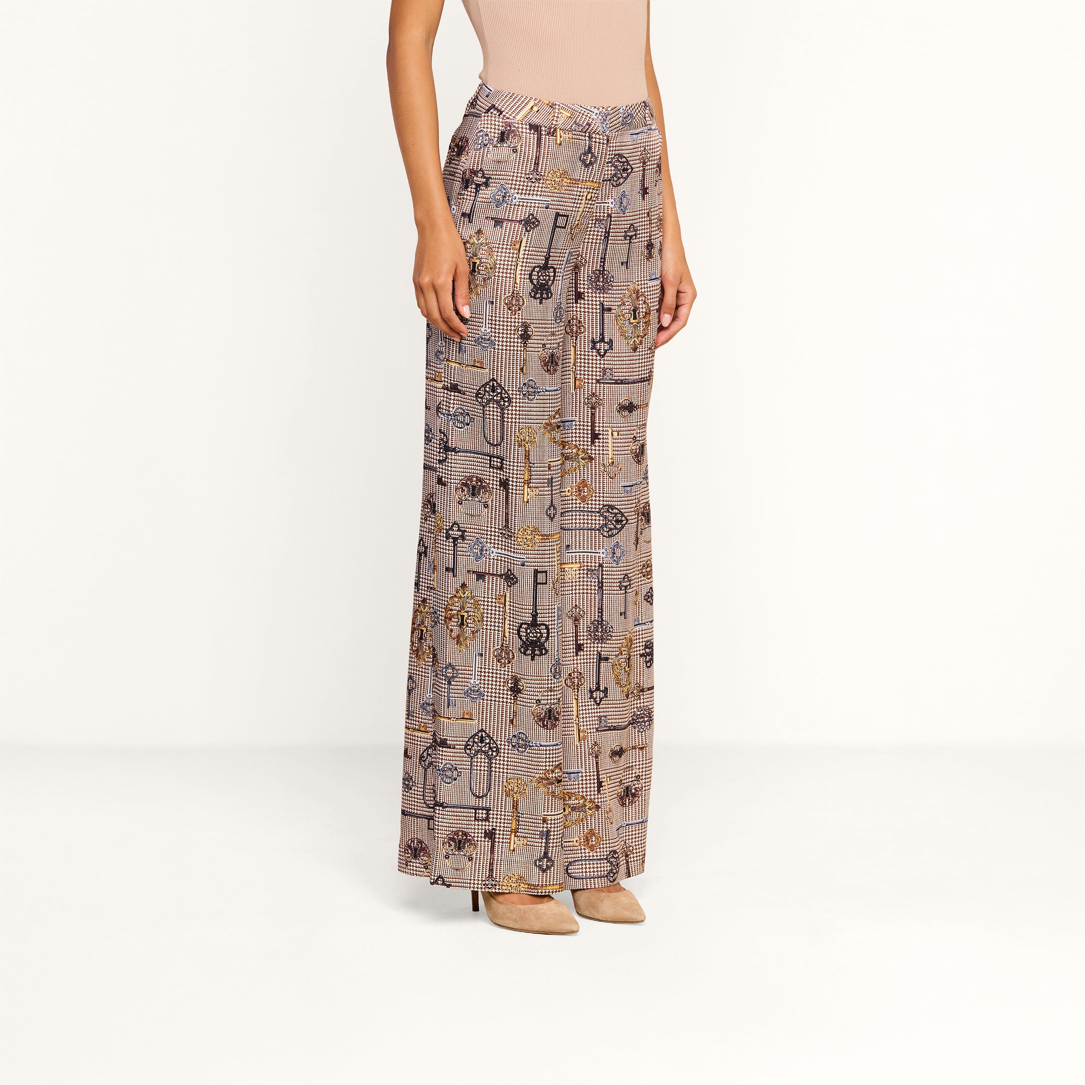 A person wearing the Pilar Wide-Leg Pant—a high-waisted, wide-leg silhouette satin jacquard trouser with various key designs—paired with a sleeveless beige top and beige heels stands against a plain white background.