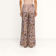 A person stands facing away, wearing the Pilar Wide-Leg Pant featuring various abstract designs, paired with a fitted, sleeveless beige top against a plain white background.