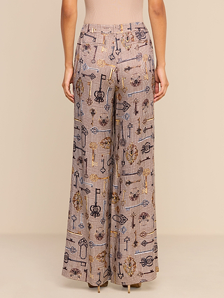 A person wearing the Pilar Wide-Leg Pant, designed with a grid pattern and musical instrument motifs, featuring a chic high-waisted, wide-leg silhouette, shown from the waist down and viewed from the back.