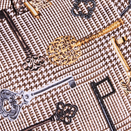 The Pilar Wide-Leg Pant is crafted from a patterned satin jacquard fabric adorned with ornate vintage keys in gold, silver, and black tones against a brown houndstooth background.