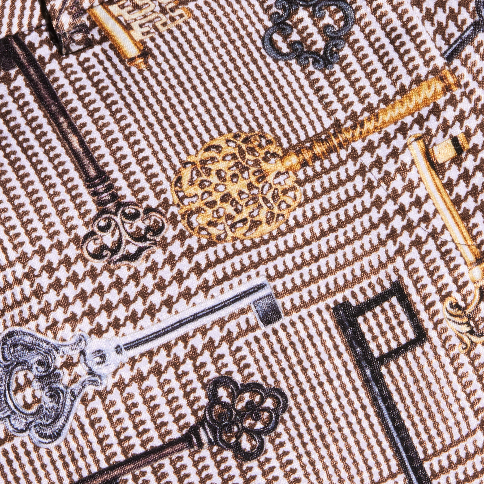 The Pilar Wide-Leg Pant is crafted from a patterned satin jacquard fabric adorned with ornate vintage keys in gold, silver, and black tones against a brown houndstooth background.