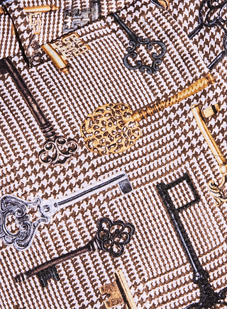 I pantaloni a gamba larga Pilar presentano un tessuto fantasia impreziosito da chiavi in stile vintage nei colori oro, argento e nero disposte in varie direzioni su uno sfondo marrone e bianco dalla trama ruvida, che evocano il fascino intramontabile dei classici pantaloni a pied-de-poule o la ricca lucentezza del jacquard satinato.