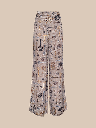 The Pilar Wide-Leg Pant features an all-over key and chain pattern set against a small checkered background, crafted from luxurious satin jacquard for an elevated look, and is showcased against a plain beige backdrop.