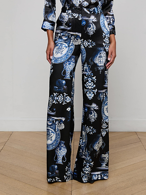 A person wearing L'AGENCE Pilar Silk Wide-Leg Pant in black with a blue and white porcelain floral print, standing on a wooden floor against a plain white wall.