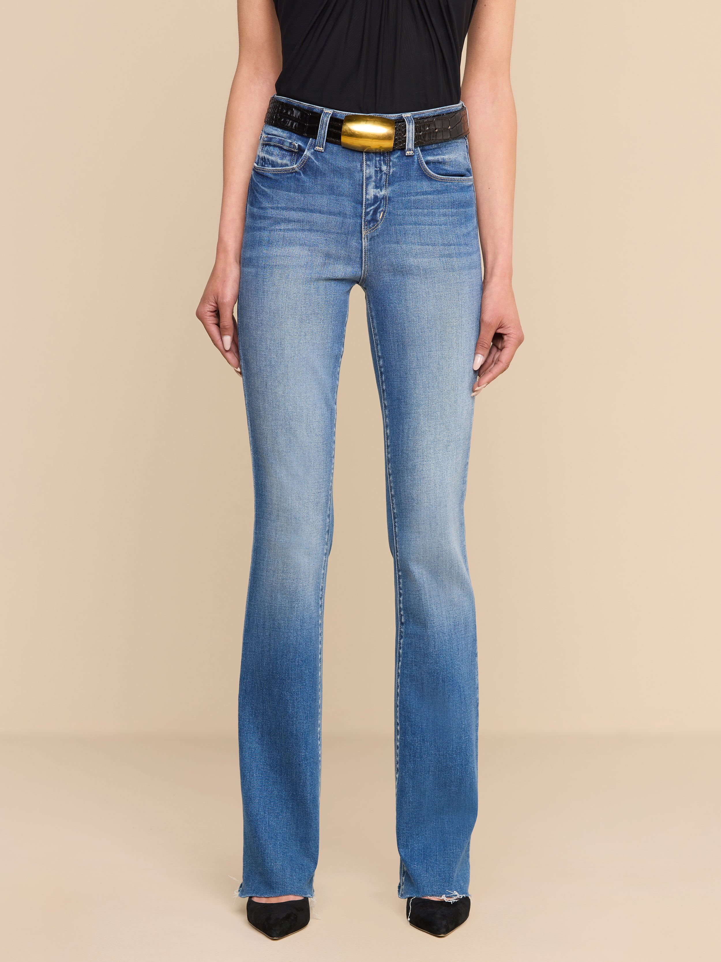 Person wearing Ruth Straight-Leg Jean in light blue—crafted from premium stretch denim—paired with a black sleeveless top, a black belt featuring a gold buckle, and black pointed shoes, standing against a plain white background.