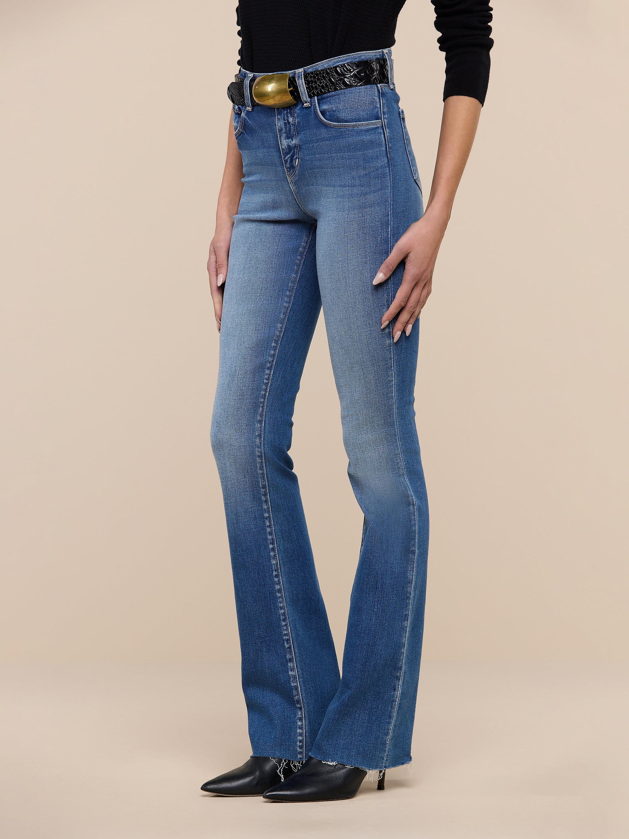 Person wearing Ruth Straight-Leg Jean in light blue, crafted from premium stretch denim. Paired with a black top, black belt, and black pointed shoes. The background is plain white, and only the lower half of the body is visible.