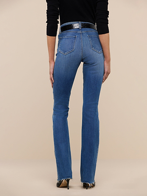 A person stands facing away, wearing Ruth Straight-Leg Jean in blue with frayed hems, a black textured belt, and a black long-sleeve top against a plain beige background.