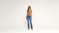 A woman wearing sunglasses, a tan sleeveless top, blue jeans, and sandals stands against a plain white background.
