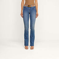 Una modella indossa i jeans Ruth Straight-Leg in classico indaco, con orlo grezzo e una leggera sfumatura sulla coscia, abbinati a una cintura marrone, un top senza maniche color cuoio e tacchi open-toe color carne, in piedi davanti a uno sfondo beige a tinta unita.