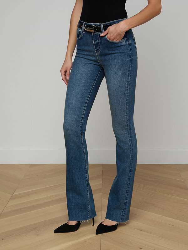 A person wearing the Ruth Straight-Leg Jean—a high-waisted indigo denim with a raw hem—paired with a brown sleeveless top and beige heeled sandals stands against a plain white background. Only the lower half of the body is visible.