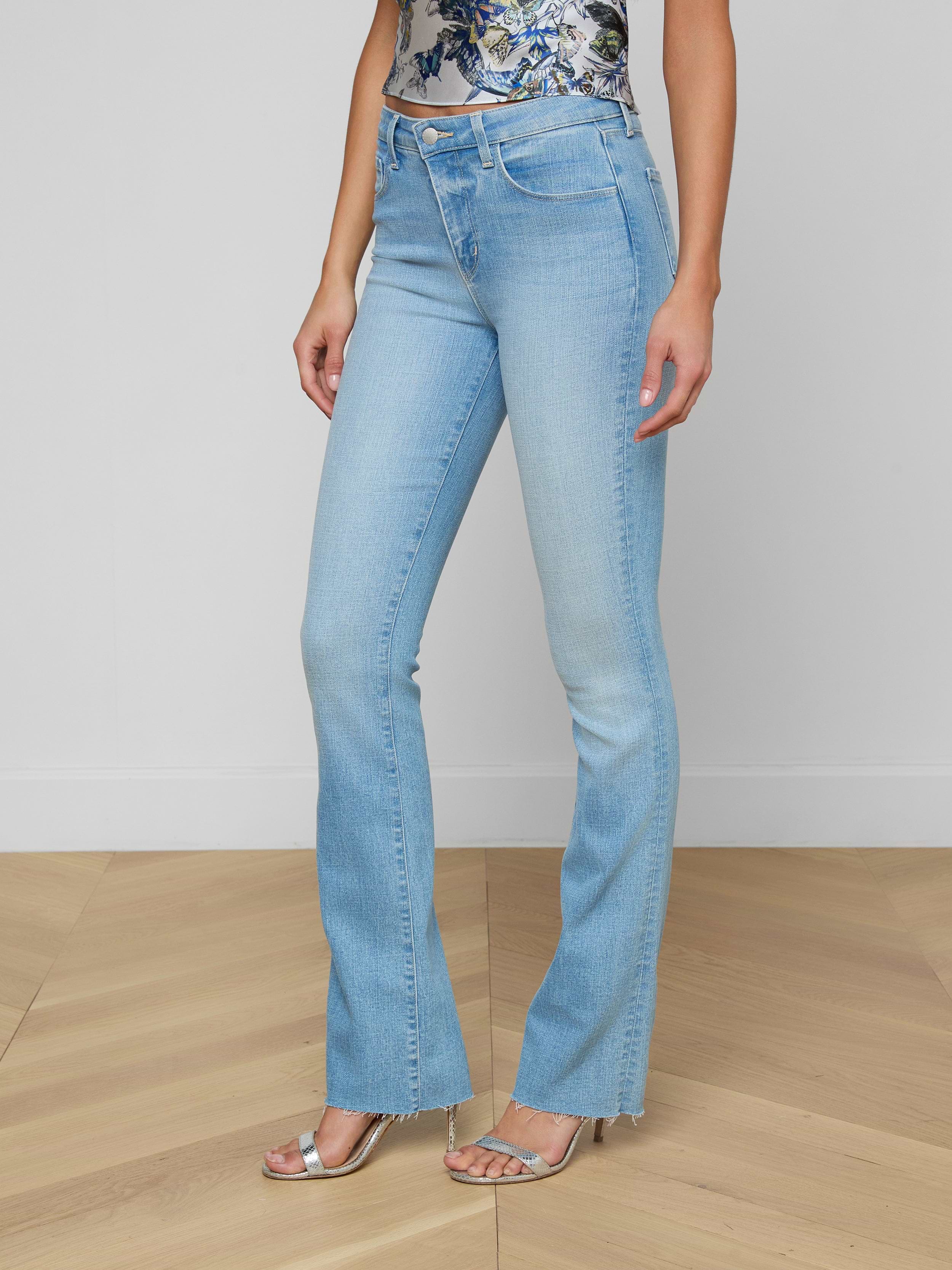 Wearing the Ruth Straight-Leg Jean in a light blue, vintage wash with slight fading, styled with a floral top and silver open-toe heels, a person stands against a plain white background.