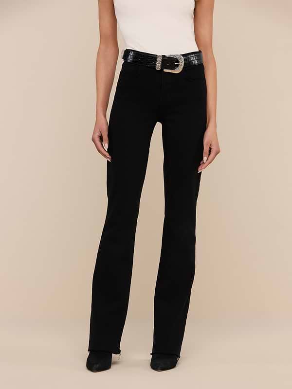 A person wearing the Ruth Straight-Leg Jean in black stretch denim, styled with a white sleeveless top, black shoes, and a black belt with a large buckle stands against a plain white background.