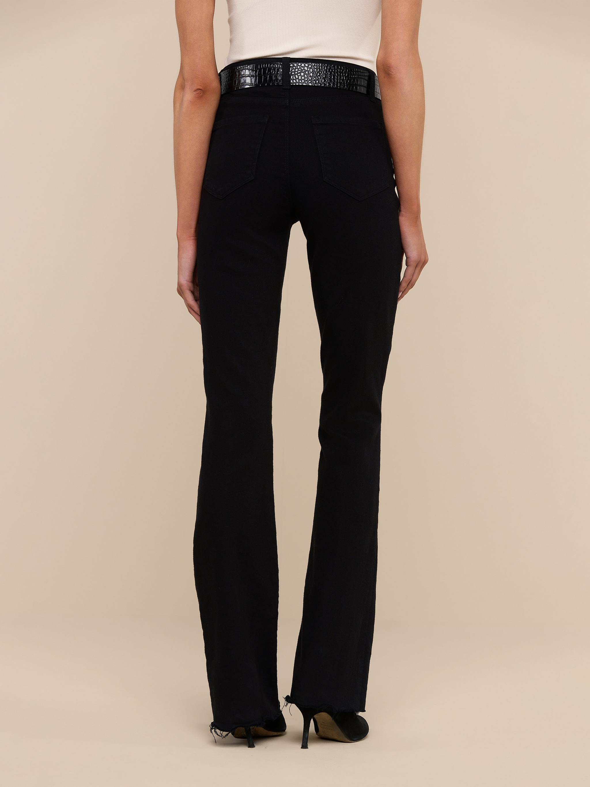 A person wearing the Ruth Straight-Leg Jean in black stretch denim, paired with a white top and black heels, stands facing away from the camera against a plain white background.