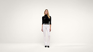 A woman with long blonde hair stands facing forward, wearing a black turtleneck top, white pants, black belt, and black shoes, against a plain white background.