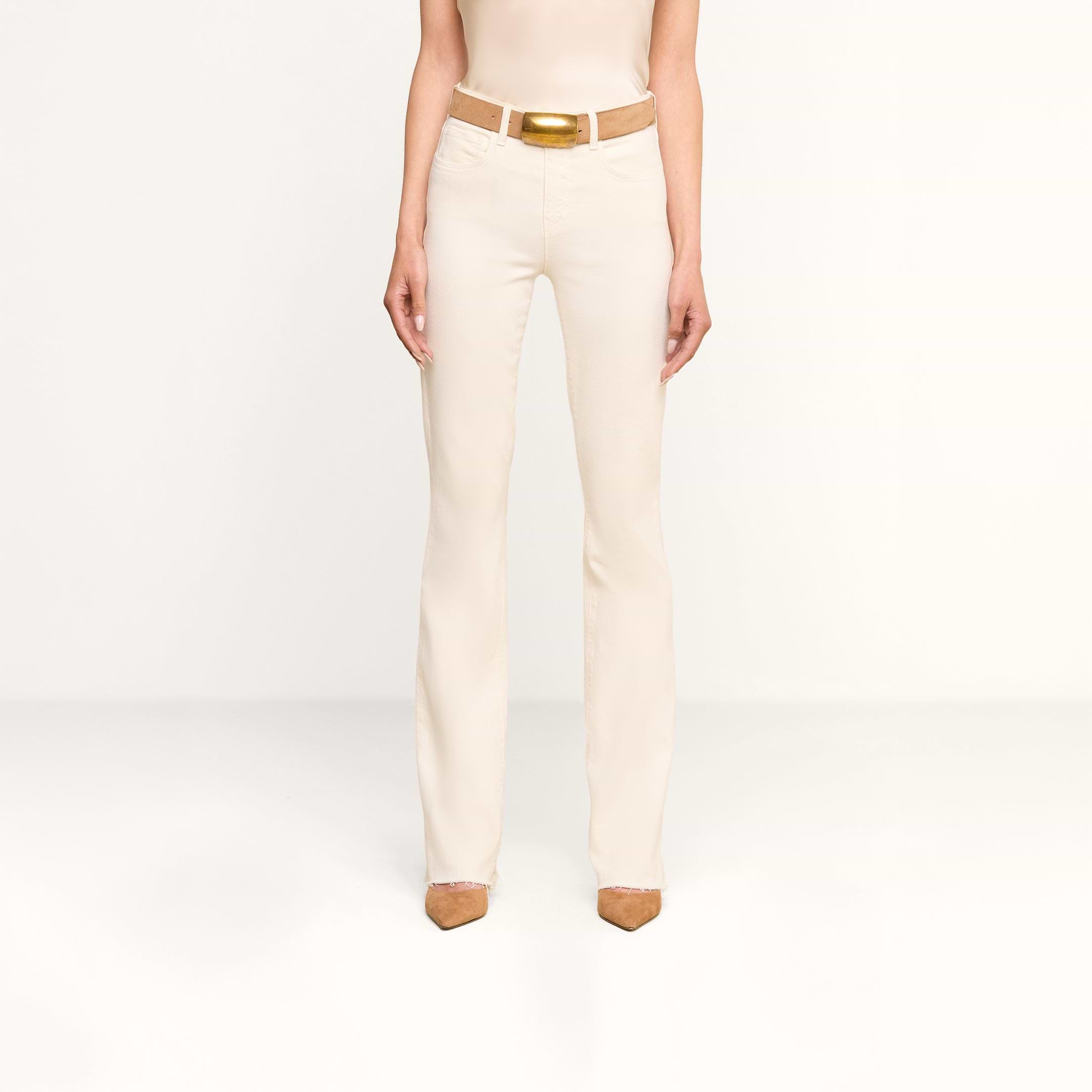 A person stands facing forward, wearing the Ruth Straight-Leg Jean in vintage white, styled with a matching cream-colored tank top, a tan belt, and brown pointed-toe shoes against a plain white background.