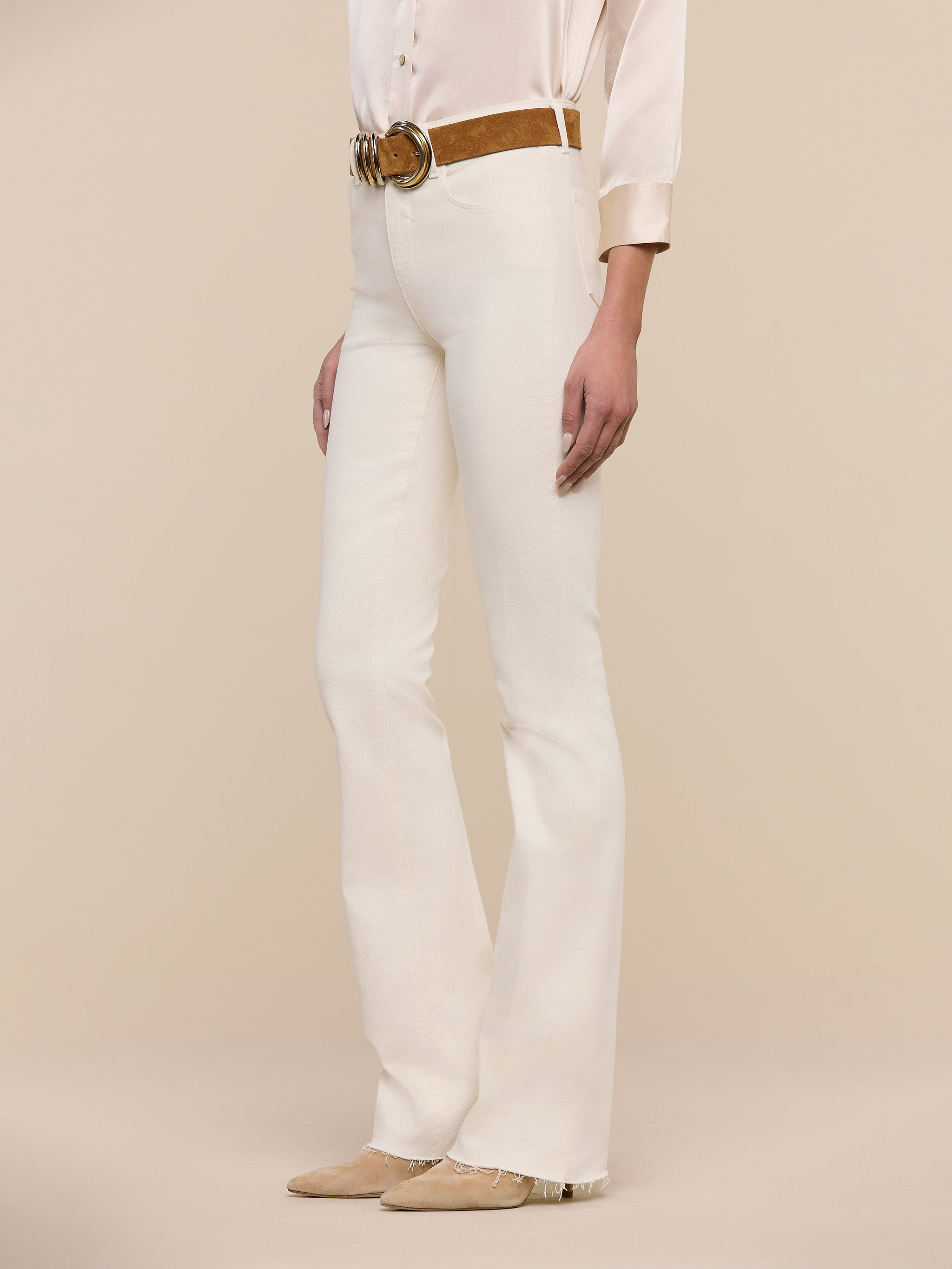 A person wearing Ruth Straight-Leg Jean in a cream shade, paired with a beige sleeveless top, a brown belt, and brown pointed-toe shoes stands against a plain white background.
