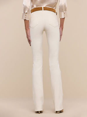 A person faces away, wearing Ruth Straight-Leg Jean in vintage white, paired with a beige belt and silky beige long-sleeve top. A neutral background highlights the jeans fit and soft, timeless color palette.