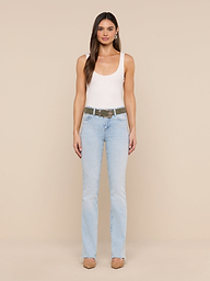 A woman stands facing forward against a plain white background, wearing a white tank top, the Ruth Straight-Leg Jean in light blue classic stretch denim with a raw hem, a belt, and beige heels.