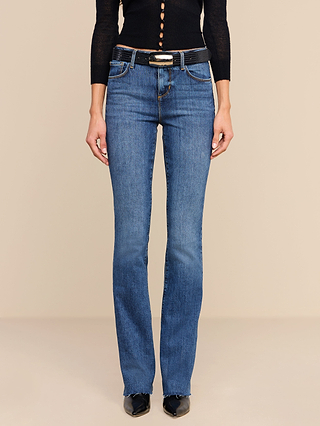 A person is wearing a black long-sleeve top, the Ruth Straight-Leg Jean in a medium indigo wash with a black belt, and black shoes, standing against a plain beige background.