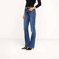 A person wearing a black long-sleeve top, a belt, black heeled boots, and the Ruth Straight-Leg Jean in medium indigo stretch denim stands against a plain white background.