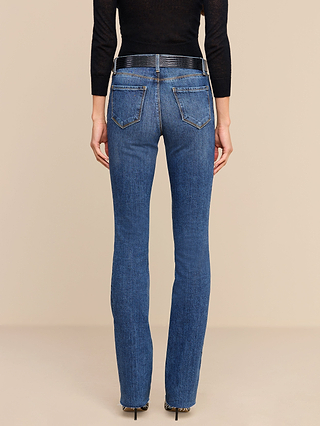 A person wearing the Ruth Straight-Leg Jean in a medium indigo wash, styled with a black belt and a black long-sleeve top, is standing facing away from the camera against a plain beige background.