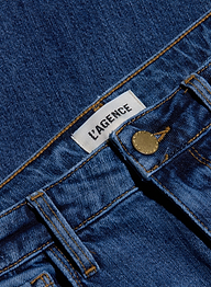 Close-up of blue stretch denim Ruth Straight-Leg Jean featuring a white LAGENCE label, a front belt loop, and a brass button. This fitted style comes in a medium indigo wash.