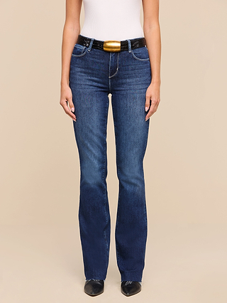 A person wearing a white sleeveless top, Ruth Straight-Leg Jean in indigo wash, a black belt with a large gold buckle, and black pointed shoes stands against a beige background.