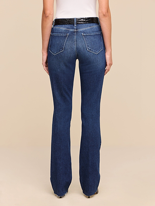 A woman stands facing away against a plain beige background, wearing a white top, a black textured belt, and the Ruth Straight-Leg Jean in dark blue indigo wash.