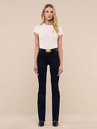 A woman stands facing forward against a plain white background, wearing a fitted white t-shirt, the Ruth Straight-Leg Jean in ultra dark indigo wash with a wide belt, and black shoes.