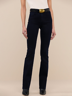 A person wearing a white sleeveless top, Ruth Straight-Leg Jean in ultra dark indigo wash, a black belt with a large gold buckle, and black shoes stands against a neutral beige background.