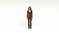 A woman wearing sunglasses, a fitted brown long-sleeve top, matching brown pants, and a large belt stands against a plain white background.