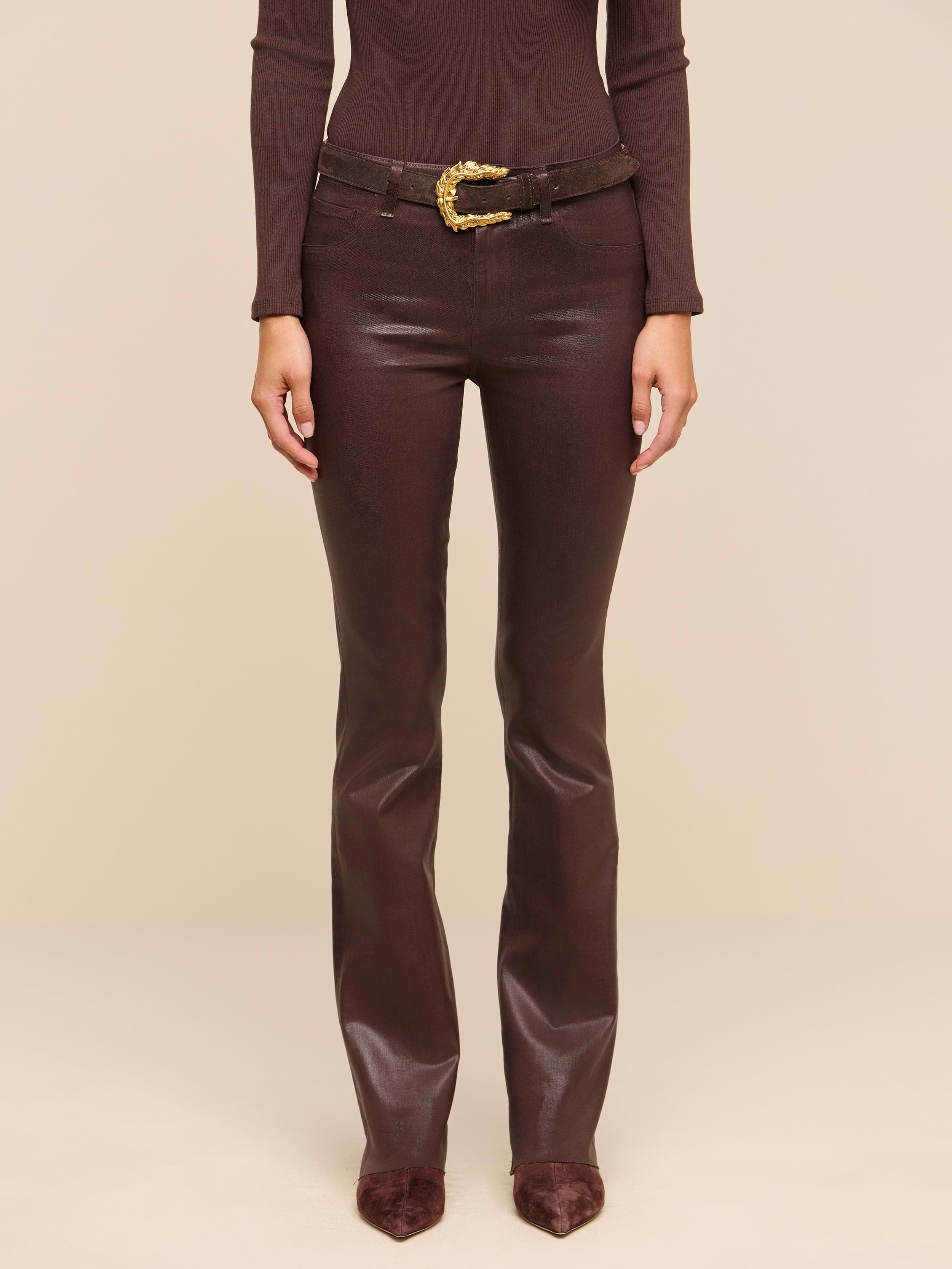 A person wearing a fitted brown long-sleeve top, the Ruth Coated Straight-Leg Jean with a gold-buckled belt, and pointed brown shoes stands against a plain white background.