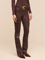 Wearing the Ruth Coated Straight-Leg Jean in brown, along with a coordinating brown long-sleeve top, a brown belt featuring a gold buckle, and pointed brown shoes, a person stands against a plain white background.