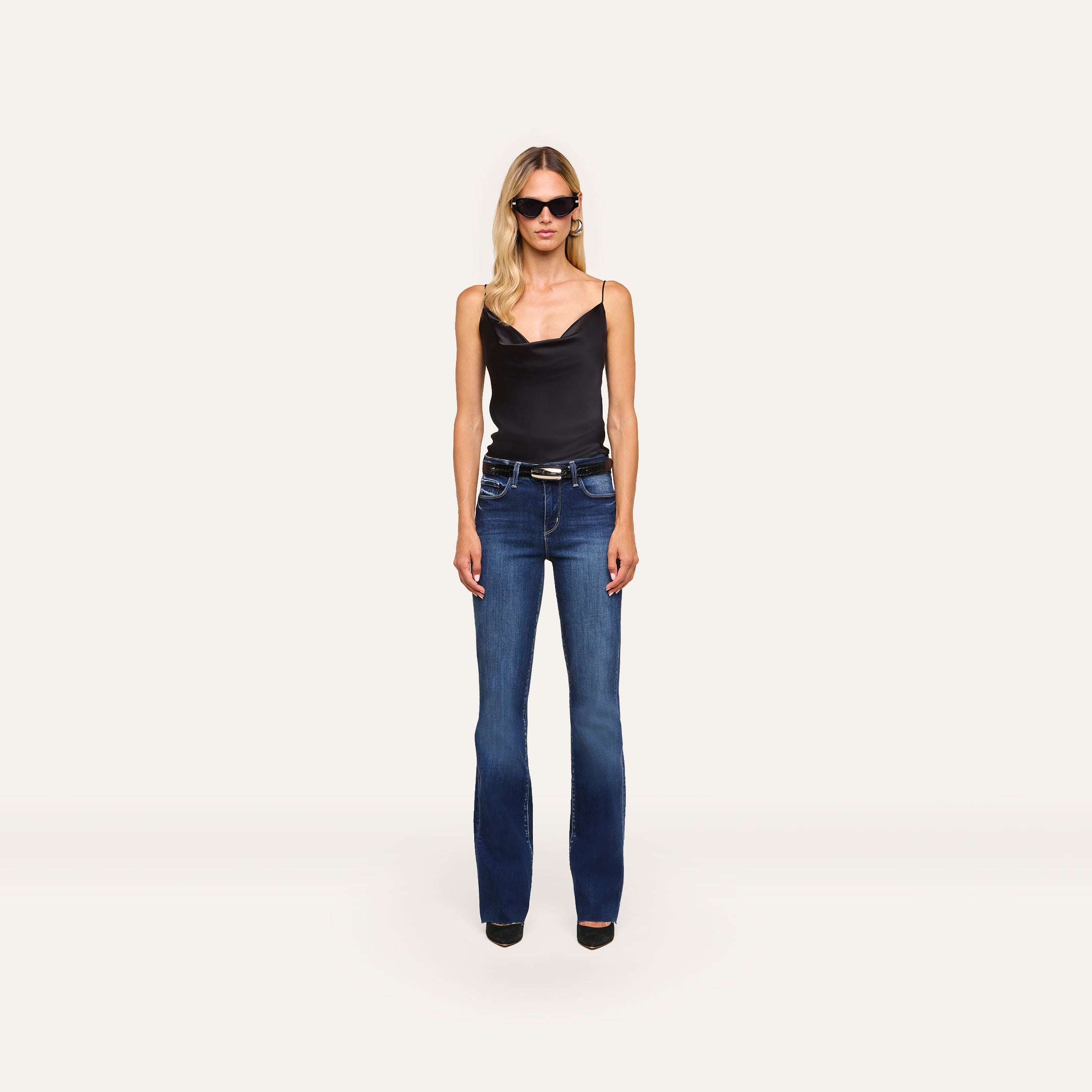 A woman in sunglasses, a black sleeveless top, and Ruth Straight-Leg Jean with black heels stands facing forward against a plain white background.