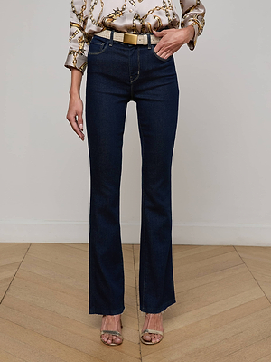 A person stands on a wooden floor wearing L'AGENCE Ruth Straight-Leg Jeans, a patterned blouse with rolled sleeves, a beige belt, and open-toe heels. The photo is cropped from the shoulders down.