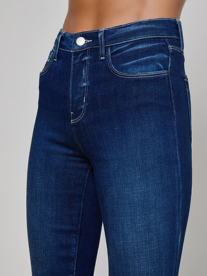 Close-up of a person wearing the L'AGENCE Ruth Straight-Leg Jean, featuring an indigo wash, white stitching, and button closure, shown from waist to mid-thigh against a plain background.