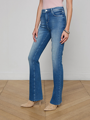 A person wearing Ruth Straight-Leg Jeans, a light pink sleeveless top, and beige pointed-toe heels stands on a wooden floor against a plain white wall. Only the lower half of the body is shown.