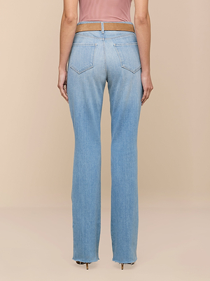Wearing the Ruth Straight-Leg Jean in light indigo with a sleeveless pink top, a person stands facing away to display the back pockets and raw hem, highlighting an effortlessly cool style.