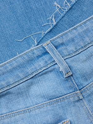 Close-up of the Ruth Straight-Leg Jean in light indigo, featuring light blue denim, a belt loop, seam stitching, and a raw frayed hem with loose threads.