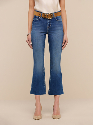 A woman models the Kendra Cropped Flare Jean against a beige background, paired with a brown belt, white top, beige heels, and a bracelet. Her arms are relaxed at her sides; her head is not shown in the image.