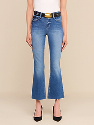 A person wearing the Kendra Cropped Flare Jean—crafted from premium stretch denim—in blue, paired with a black belt featuring a gold buckle, a white top, and black pointed heels, stands against a plain white background. Only the lower half of the body is visible.