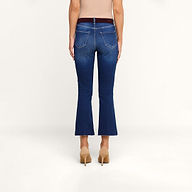 Une personne portant un jean évasé court « Kendra » bleu, assorti dun haut beige clair et descarpins beiges, se tient de dos face à lappareil photo, devant un fond beige uni.