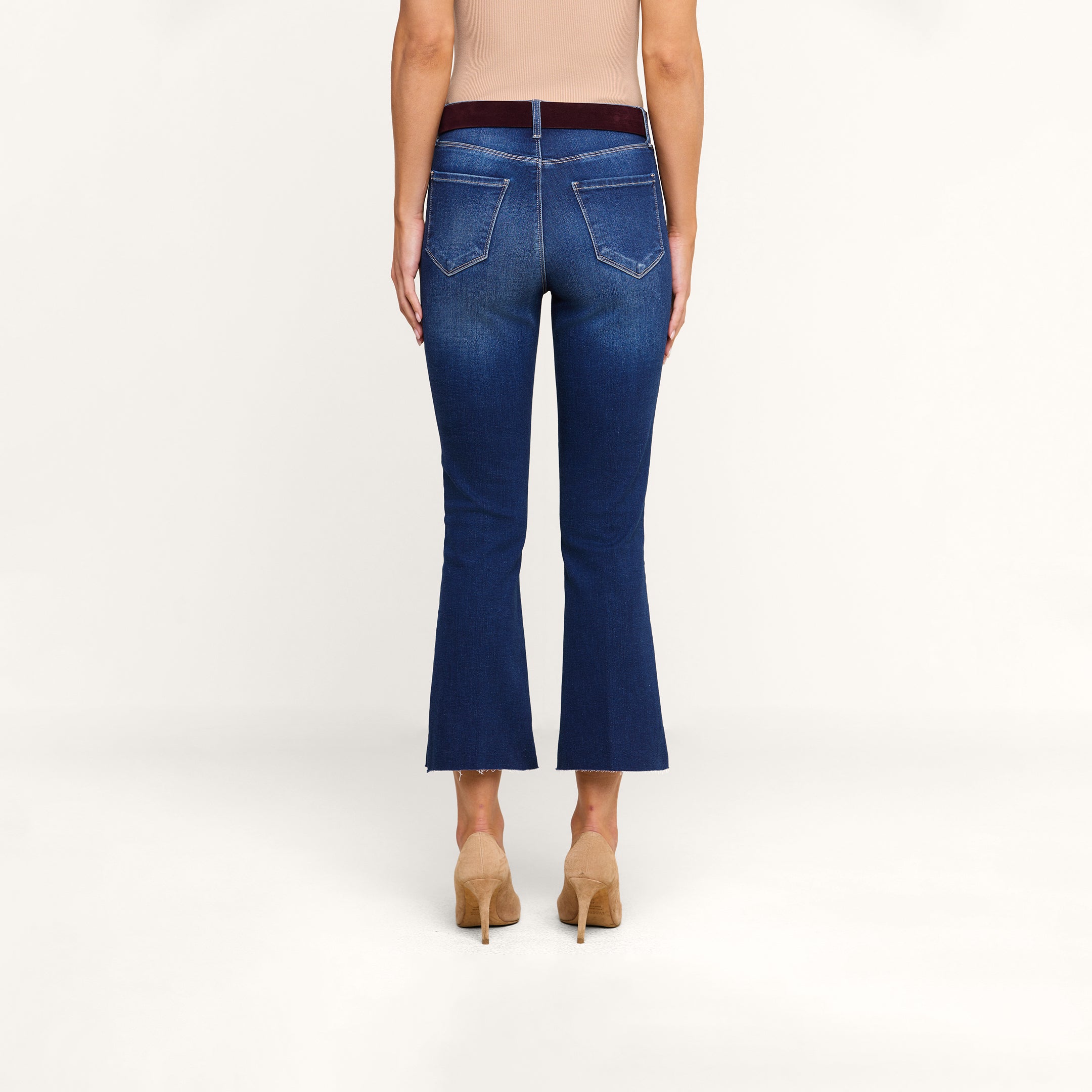 Une personne portant un jean évasé court « Kendra » bleu, assorti dun haut beige clair et descarpins beiges, se tient de dos face à lappareil photo, devant un fond beige uni.