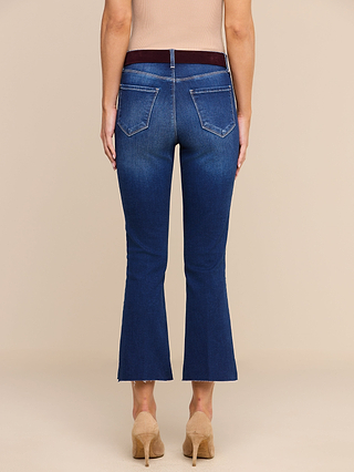 A person wearing the Kendra Cropped Flare Jean in blue, paired with a tan top and beige heeled shoes, is standing facing away from the camera against a plain beige background.